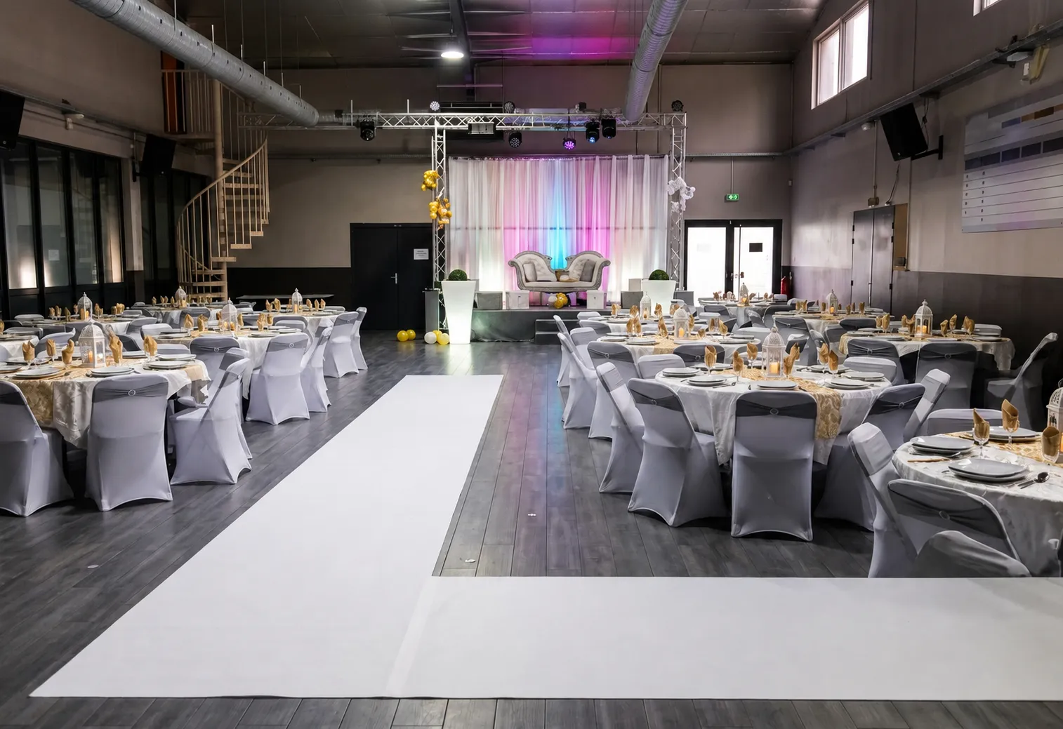 Salle de réception dressée pour un mariage avec tables rondes et estrade